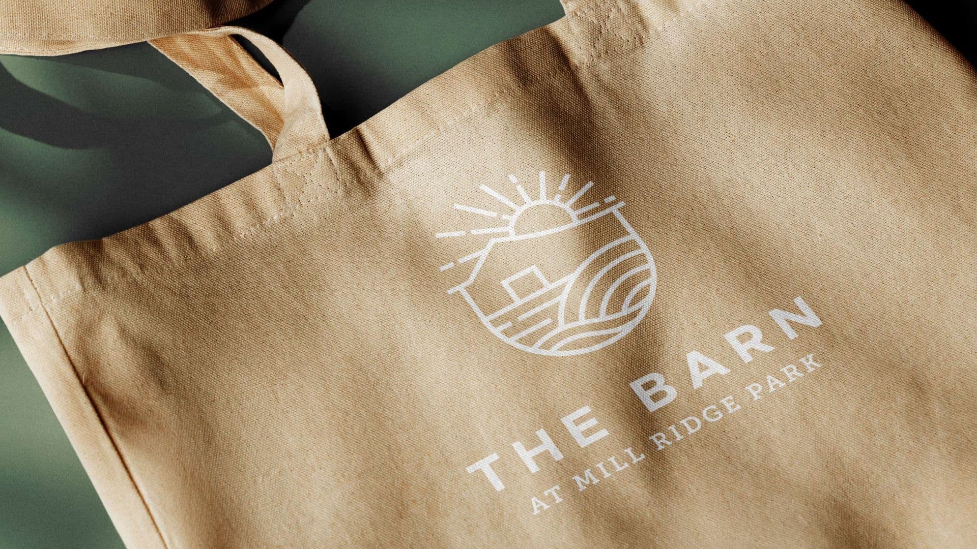 Canvas tote bag featuring "The Barn at Mill Ridge Park" sun and landscape line-art logo.