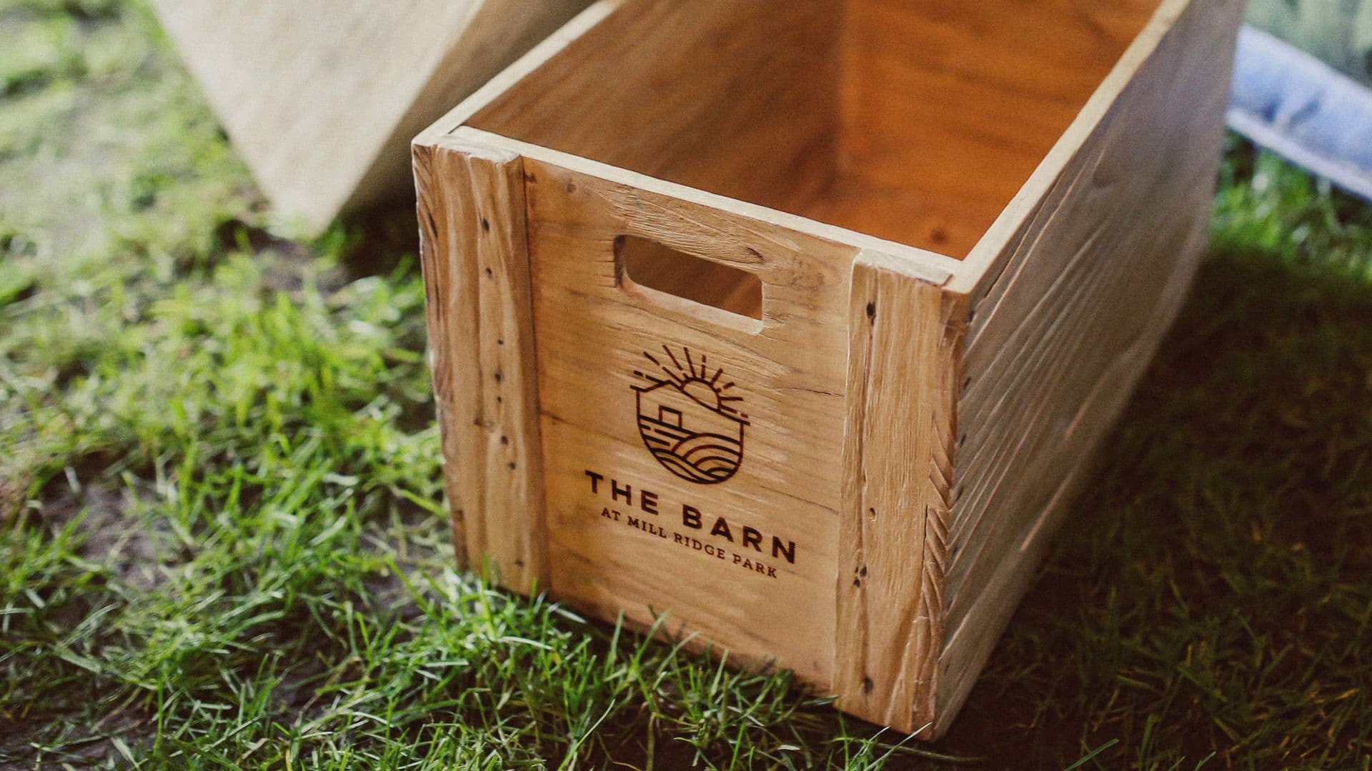 Rustic wooden crate branded with The Barn at Mill Ridge Park logo sitting on grass.