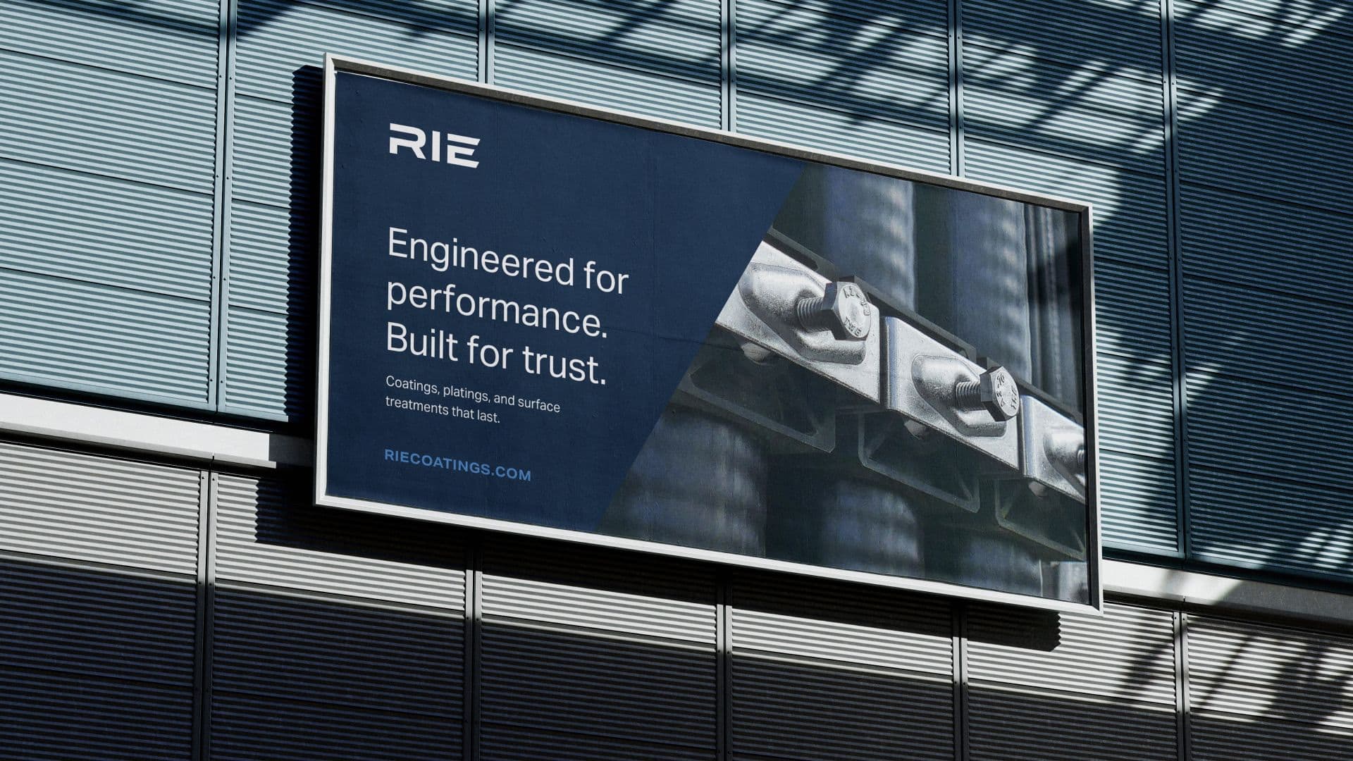 Billboard advertisement for RIE featuring industrial bolts on a dark blue background with the tagline 'Engineered for performance. Built for trust.' Promotes coatings, plating, and surface treatments with the website RIECOATINGS.COM.